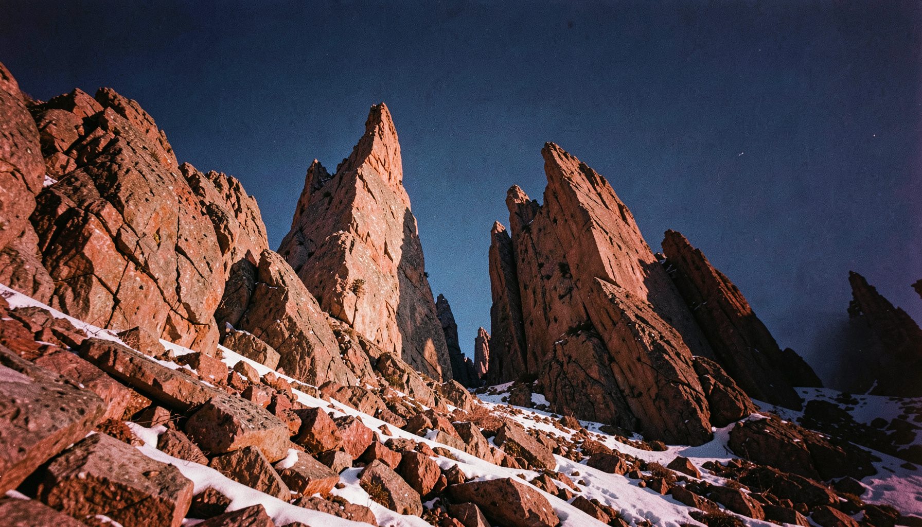 Altas agujas rocosas recortadas contra un cielo azul profundo, sobre una ladera de bloques y nieve